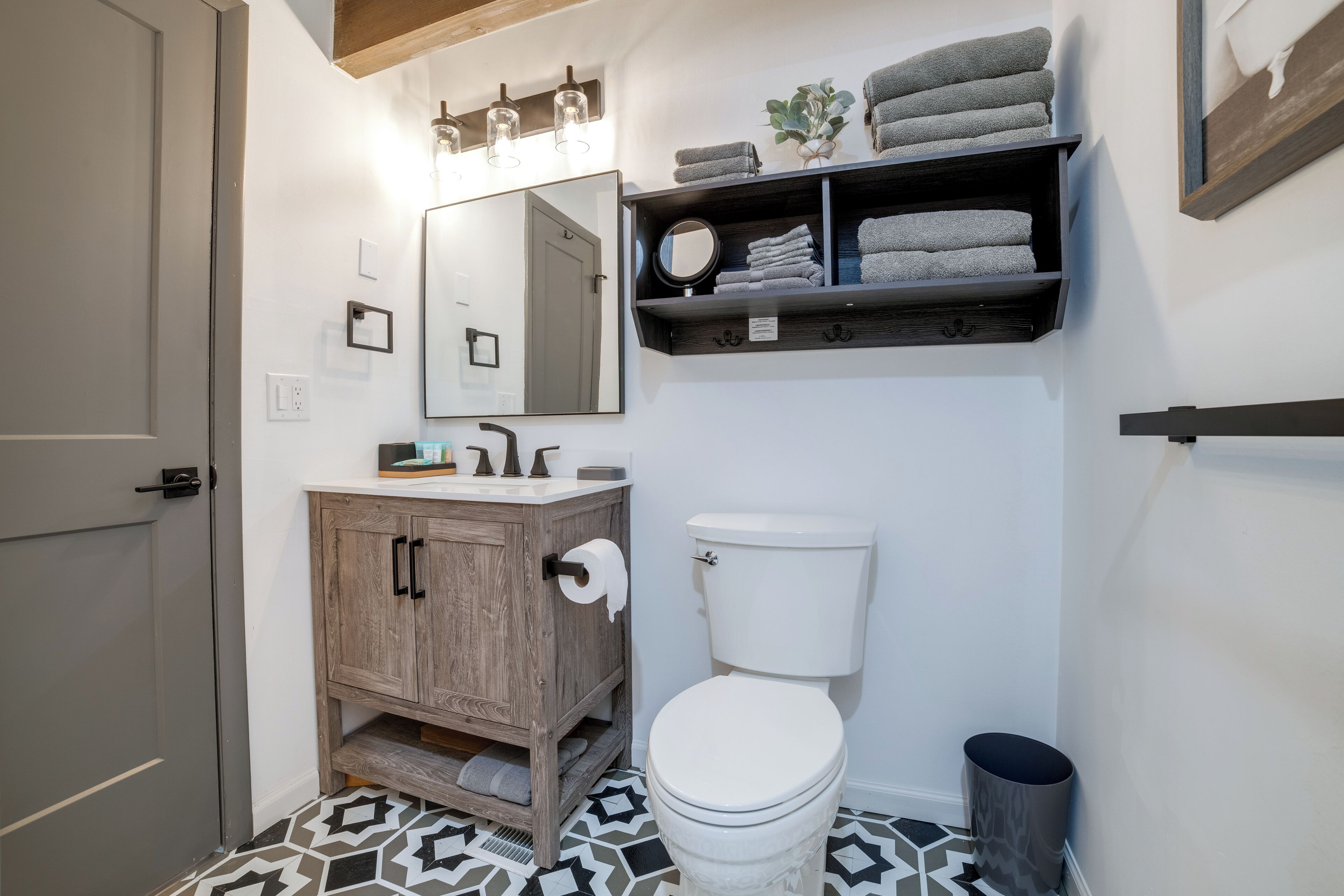 A bathroom with a wooden vanity, white toilet, and a shelf with towels.