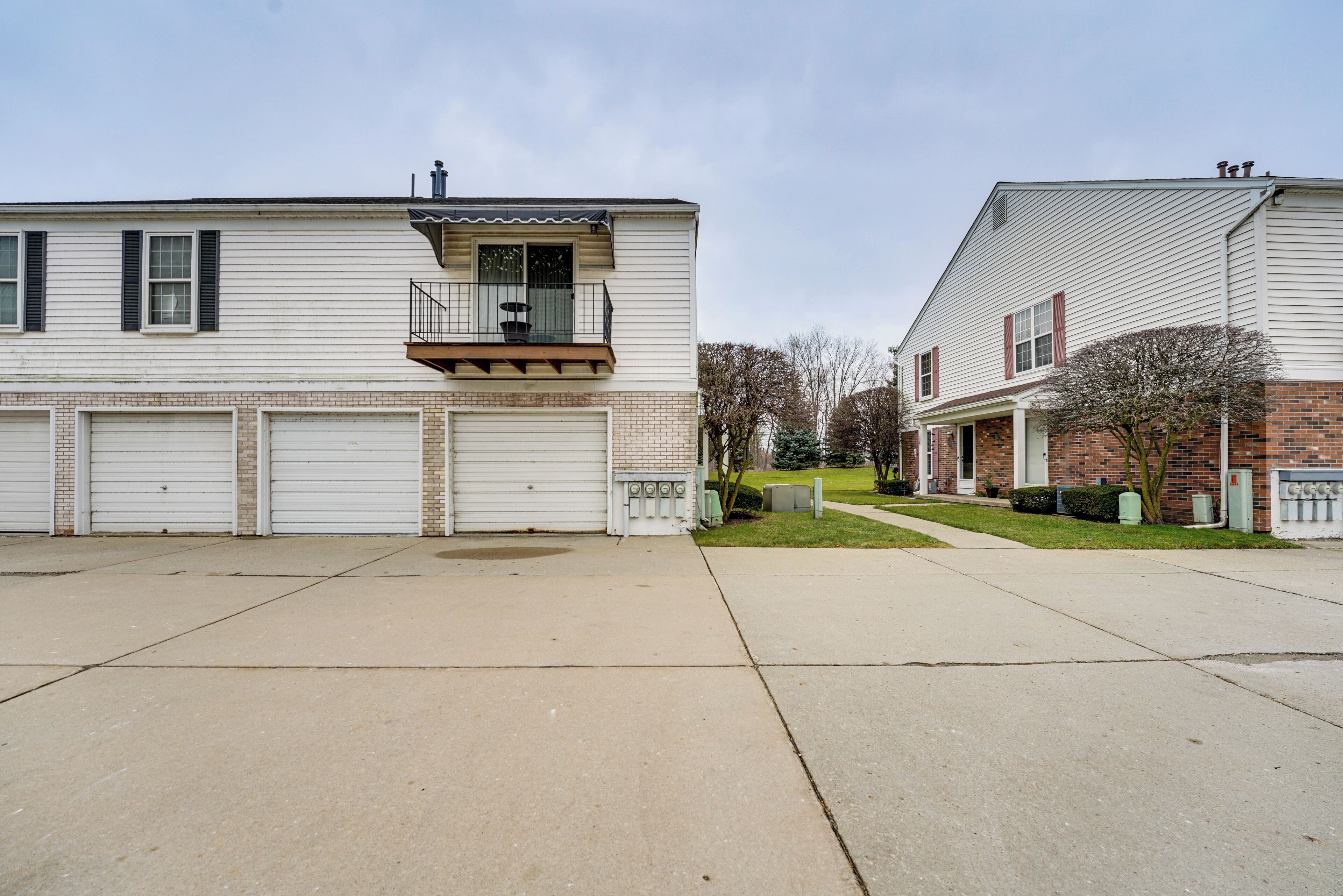 A two-story residential building with a balcony on the second floor, two garages, and a brick facade.