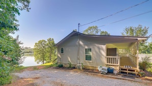 A single-story house with a covered porch, a gravel driveway, and a lake in the background. - Lakefront Getaway w/ Porch in Athens Area! (Statham)