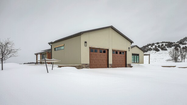 A two-story building with a garage, a covered porch, and a snow-covered landscape. - Pet-friendly Fairfax Cabin Near Missouri River! (Fairfax)