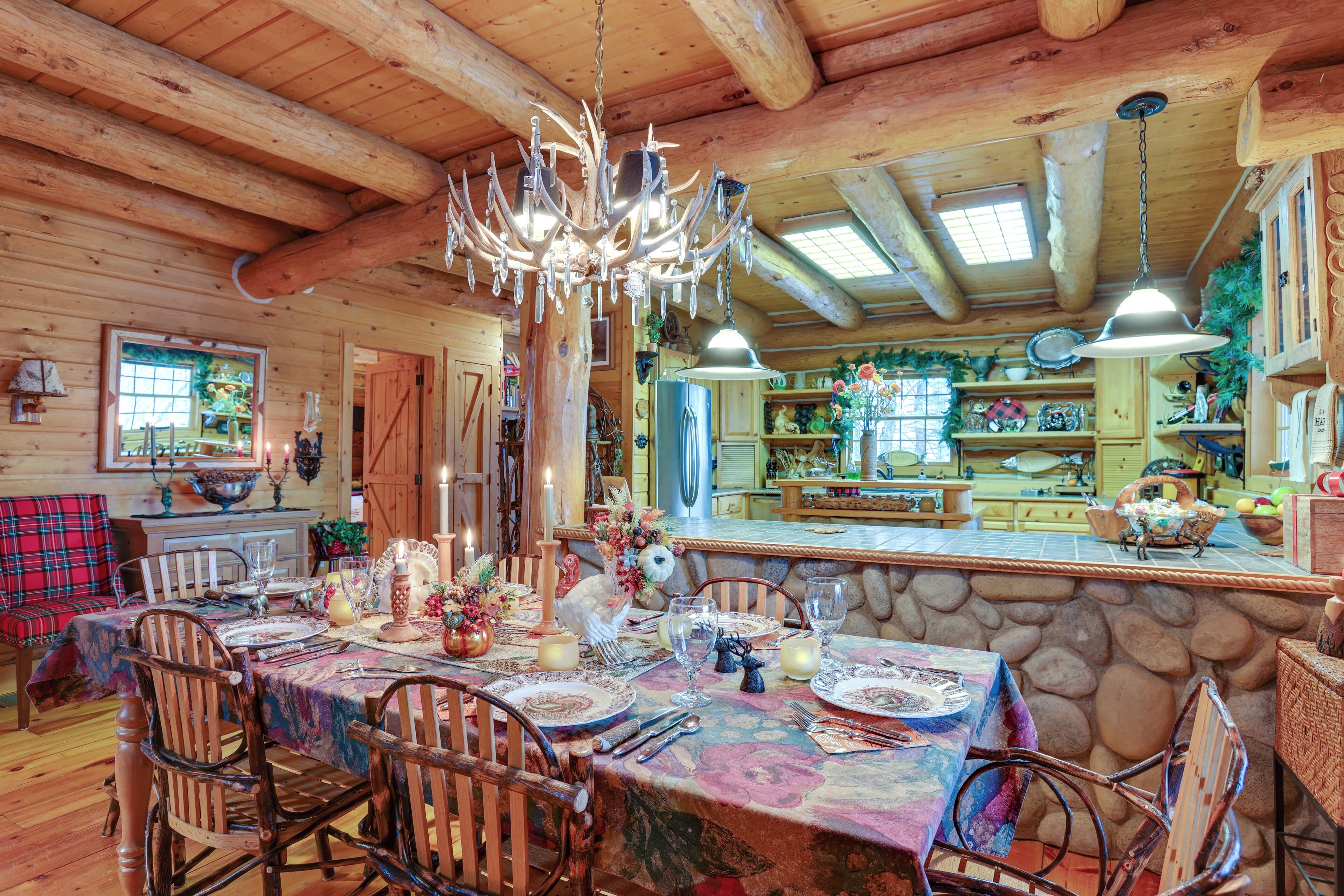 A rustic dining area with a long table set for a meal, wooden chairs, and a chandelier.