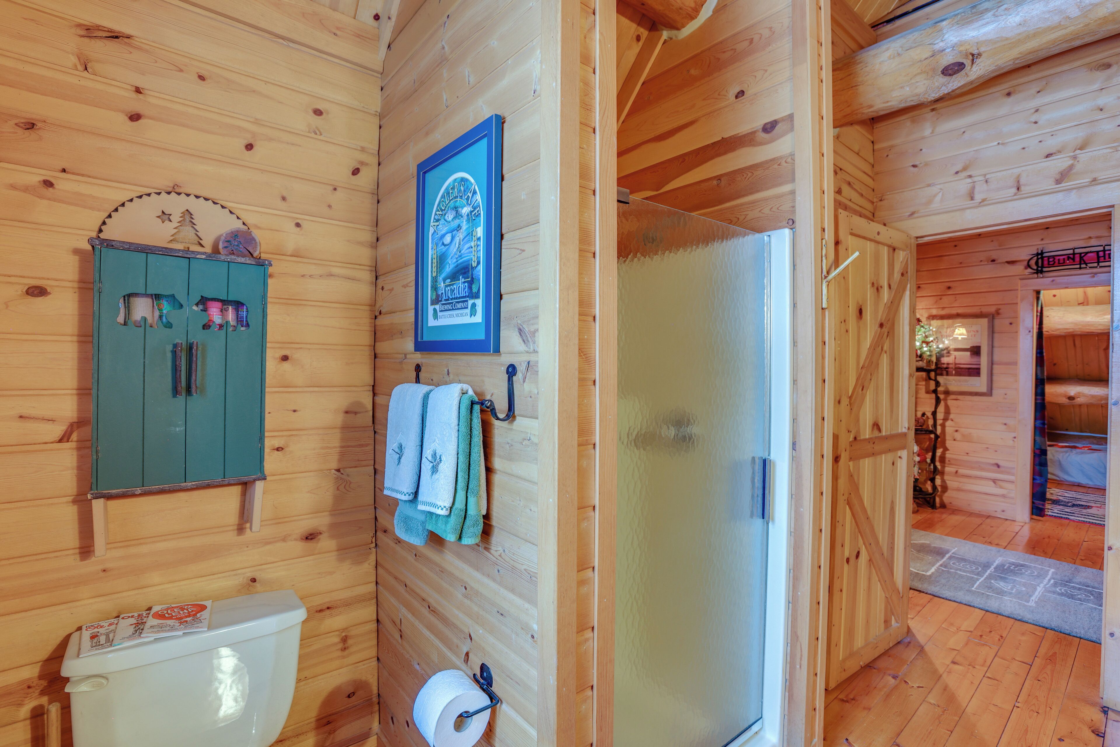 L’intérieur d’une cabane en bois comprend des toilettes, un meuble avec des serviettes, un tableau encadré et une porte en verre donnant sur une autre pièce.