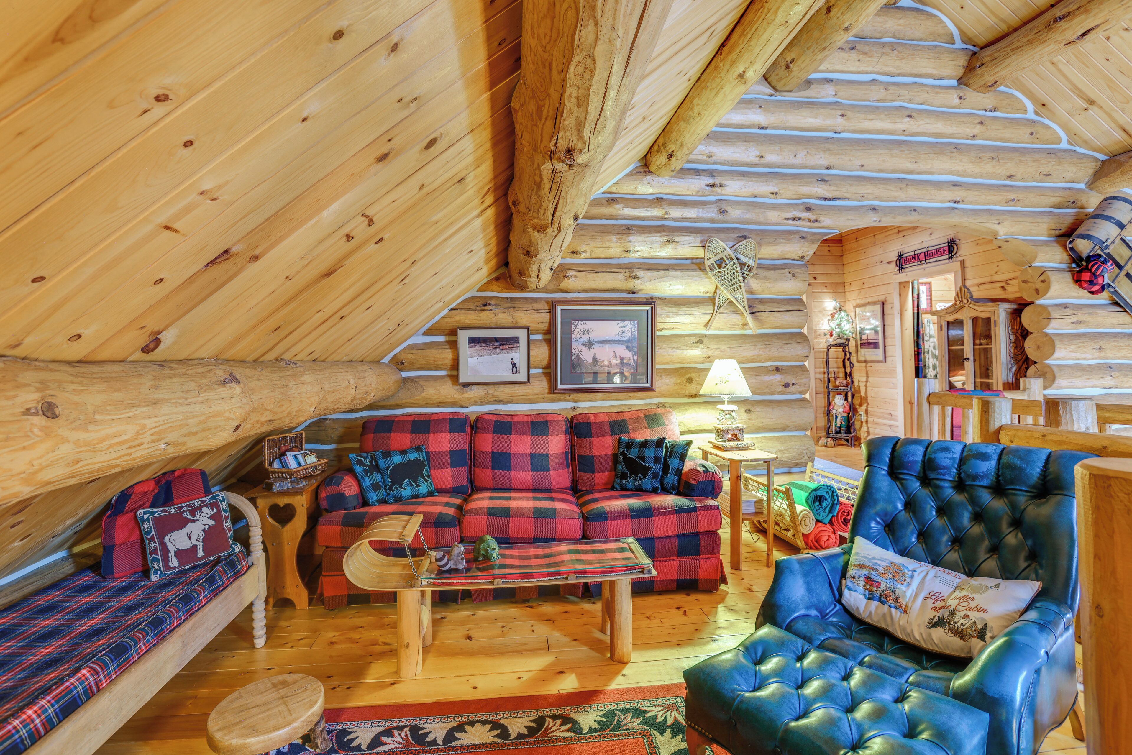 A cozy log cabin interior with a plaid sofa, a tufted armchair, and a wooden coffee table.