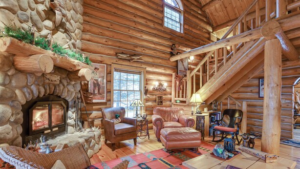 L’intérieur d’une cabane en rondins, avec une cheminée en pierre, des meubles en cuir et un escalier en bois.