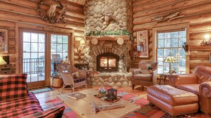 L’intérieur d’une cabane en rondins, avec une cheminée en pierre, des meubles en cuir et un coin chaleureux autour du foyer.