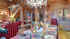L’intérieur d’une cabane en rondins, avec une table à manger dressée pour le repas, une cheminée et un escalier menant à l’étage supérieur.