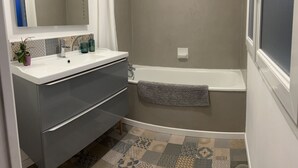 Un baño con un lavamanos blanco, muebles de color gris oscuro, ducha y baldosas de suelo estampadas.