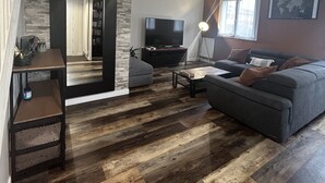 Una sala de estar moderna con una pared de acento de piedra, un sofá gris, un televisor de pantalla plana y piso de madera.