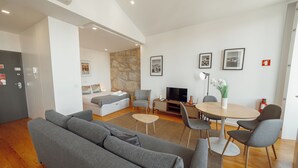 A modern living room with a grey sofa, a small round table, and a TV. There is a stone wall and a bed in the background. - Courtyard Oporto Design Apartments (Porto)