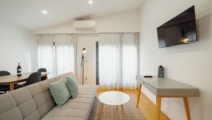 A modern living room with a sofa, a round table, a TV mounted on the wall, and a dining area with a table and chairs. - Courtyard Oporto Design Apartments (Porto)