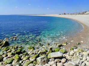 A beach with clear water, pebbles, and a distant shoreline.