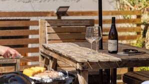 Een houten tafel met een fles wijn, twee glazen en een grill met mais erop.
