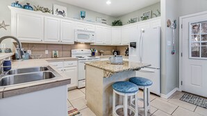 A modern kitchen with white cabinets, a granite countertop, and a built-in island with bar stools. - Made In The Shade Rp808 3 Bedroom Home by RedAwning (Rockport)