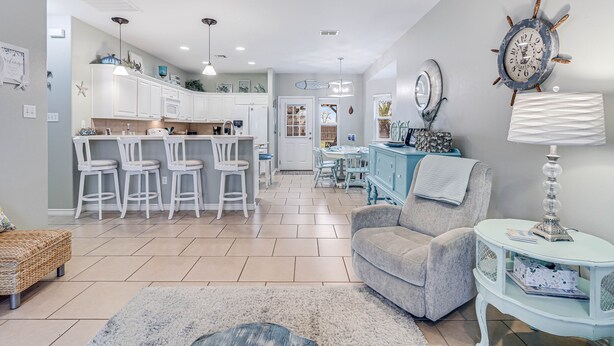 A modern kitchen with white cabinets, a dining area with a table and chairs, and a living room with a sofa and a lamp. - Made In The Shade Rp808 3 Bedroom Home by RedAwning (Rockport)