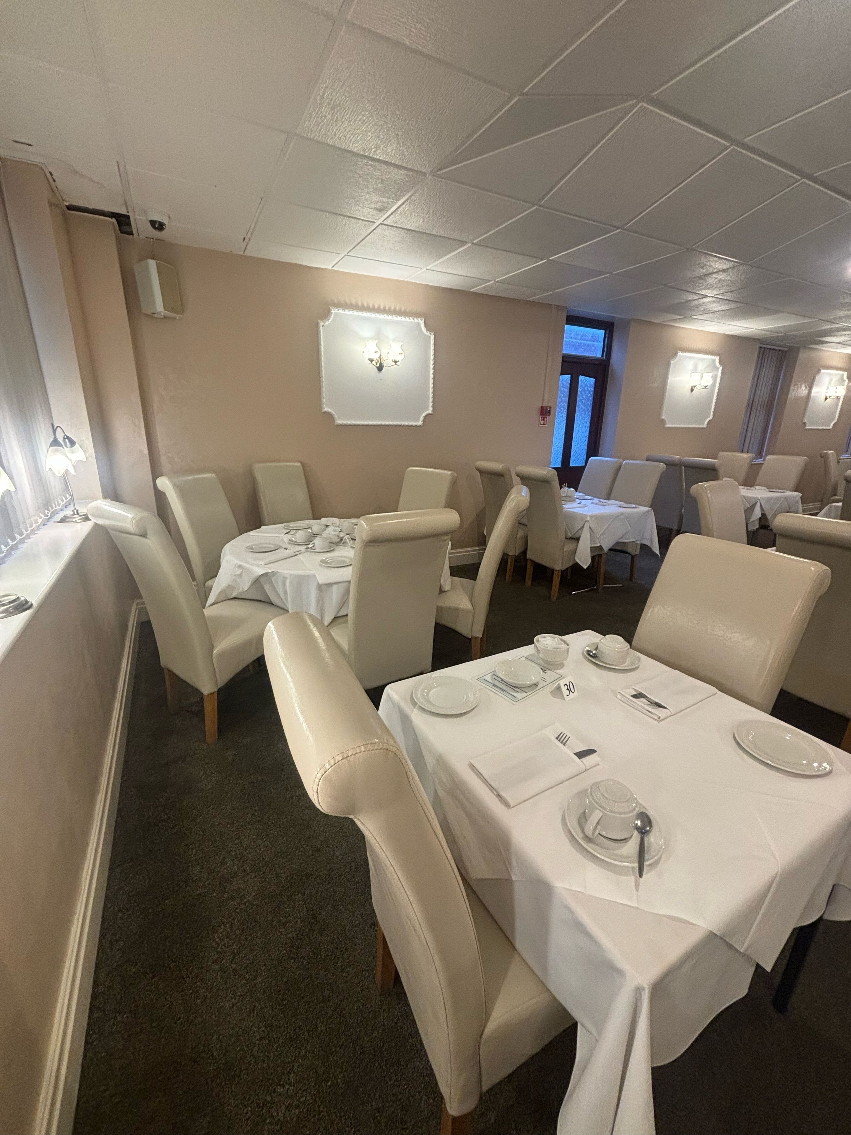 Un espace repas avec des tables dressées pour quatre personnes, chacune étant recouverte d’une nappe blanche et agrémentée de couverts en argent.