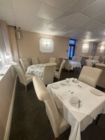 Een eetruimte met tafels voor vier personen, elk met een witte tafelkleed en bestek.