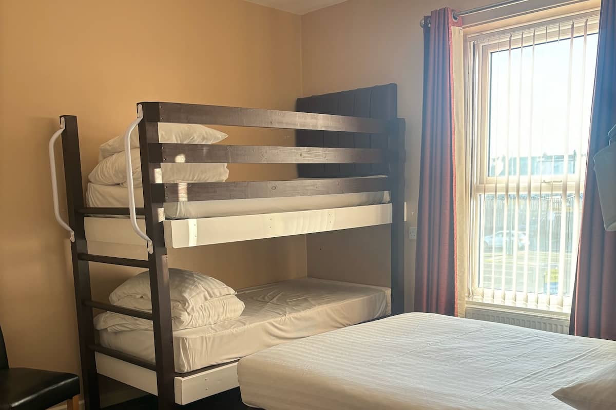 A bunk bed room with a desk and a window with curtains.