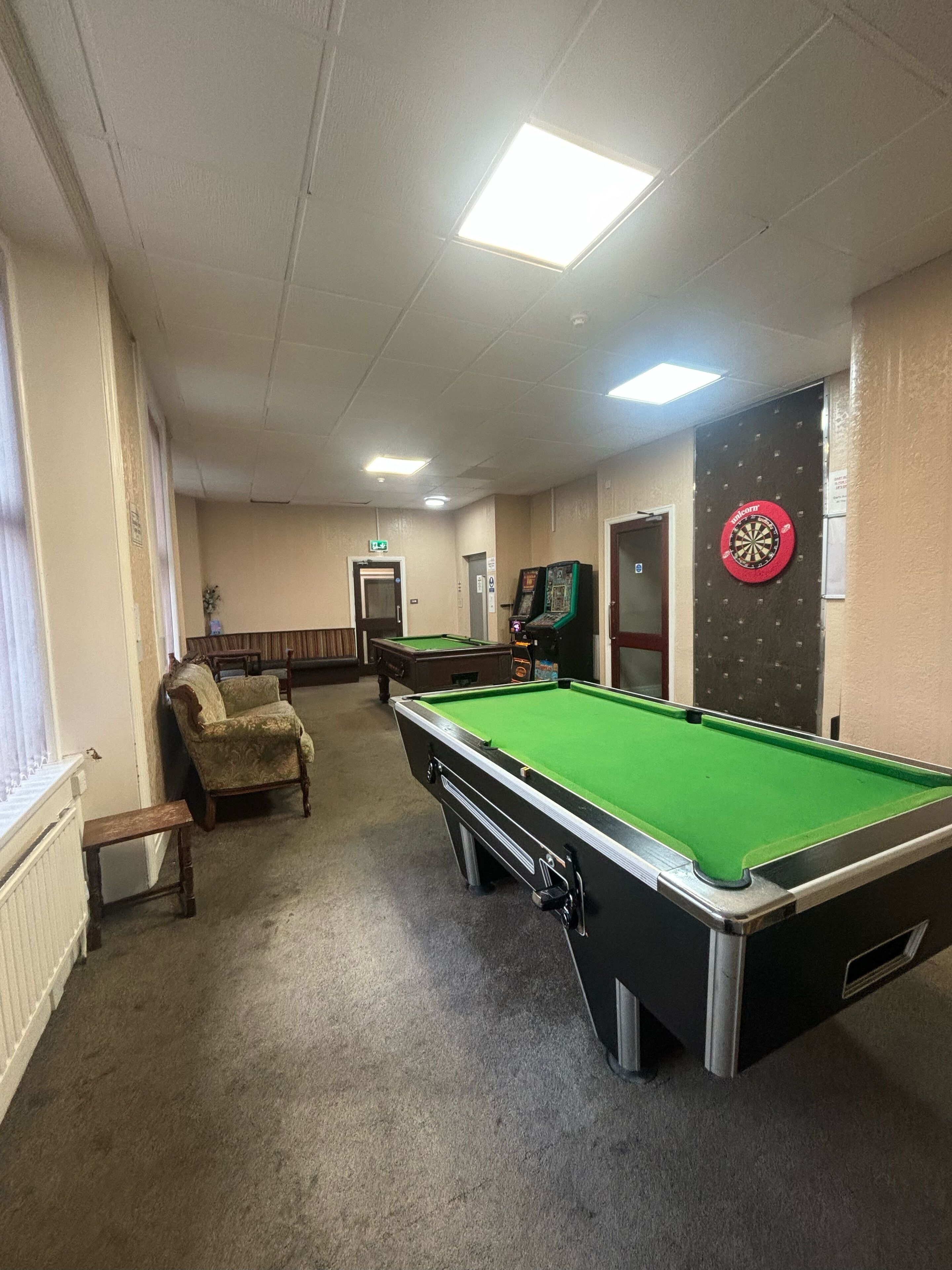 Een biljartkamer met een pooltafel, een dartbord, en een pooltafel op de achtergrond.