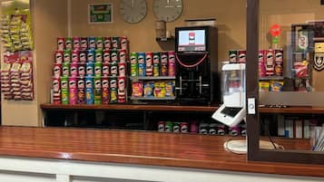 Un bar de aperitivos con una variedad de productos envasados, bebidas, una máquina de café y relojes en la pared.