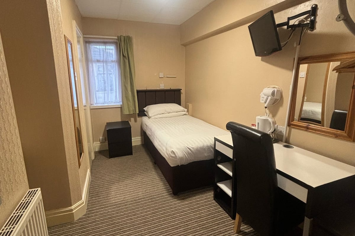 A hotel room with a bed, a desk, a chair, a TV, and a window with curtains.