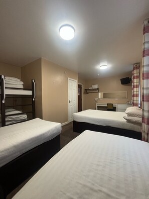 A hotel room with two single beds, a bunk bed, a desk with a chair, a mirror, and a television. - The Beechfield Hotel (Blackpool)
