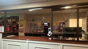 A reception area with a counter, a computer, and shelves stocked with snacks. - The Beechfield Hotel (Blackpool)