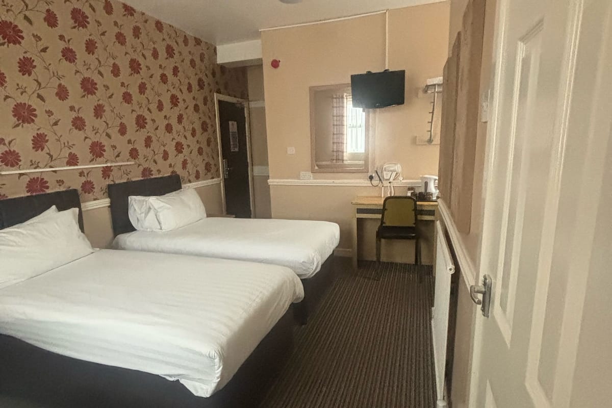 A hotel room with two beds, a desk, a chair, a television, and a window.