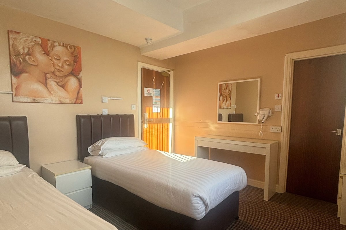 A hotel room with two beds, a desk, a mirror, and a painting on the wall.