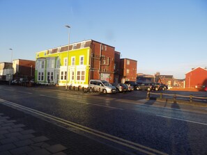 A street with parked cars and buildings, including a brightly colored building with white and green facades. - The Beechfield Hotel (Blackpool)