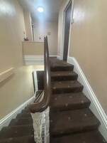 Eine Treppe mit Handlauf, Teppichstufen und einer Empfangsebene mit Ablagefläche.
