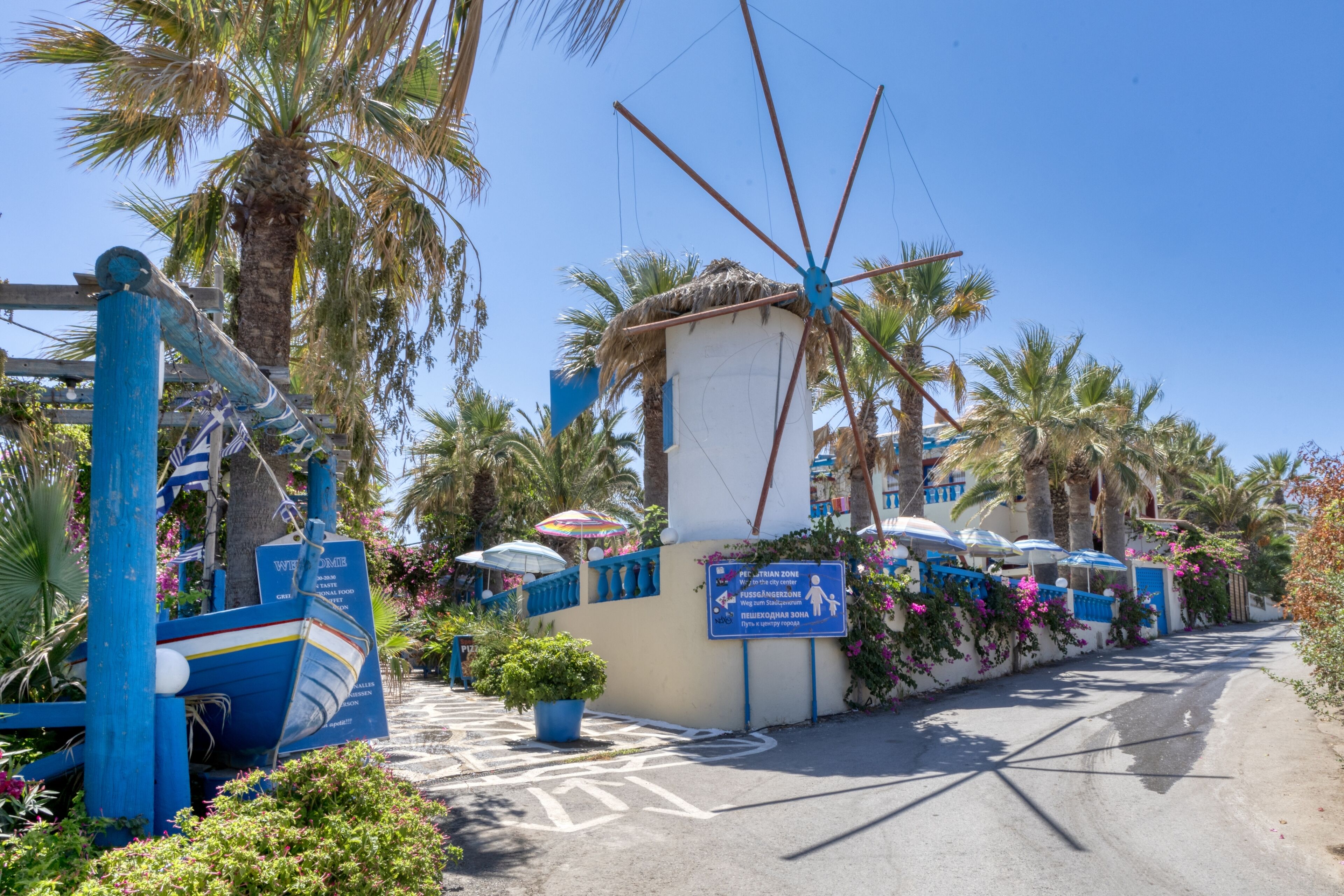 A coastal area with a blue boat sculpture, palm trees, and a sign indicating a beach area.