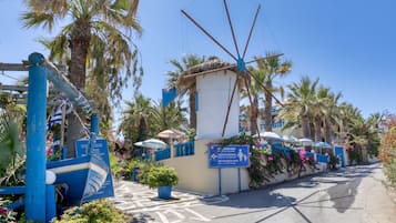A coastal area with a blue boat sculpture, palm trees, and a sign indicating a beach area.