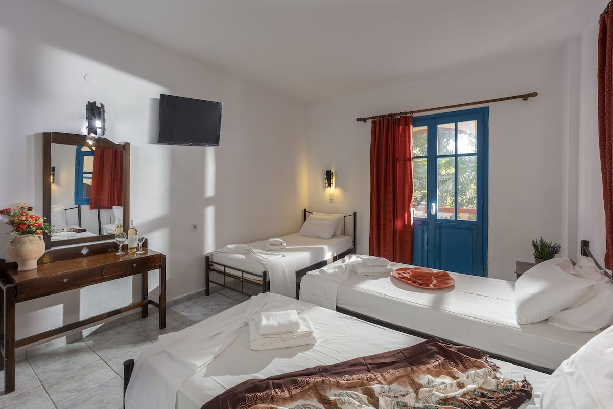 A hotel room with two beds, a sofa, a wooden desk, a flat-screen TV, and a window with red curtains.