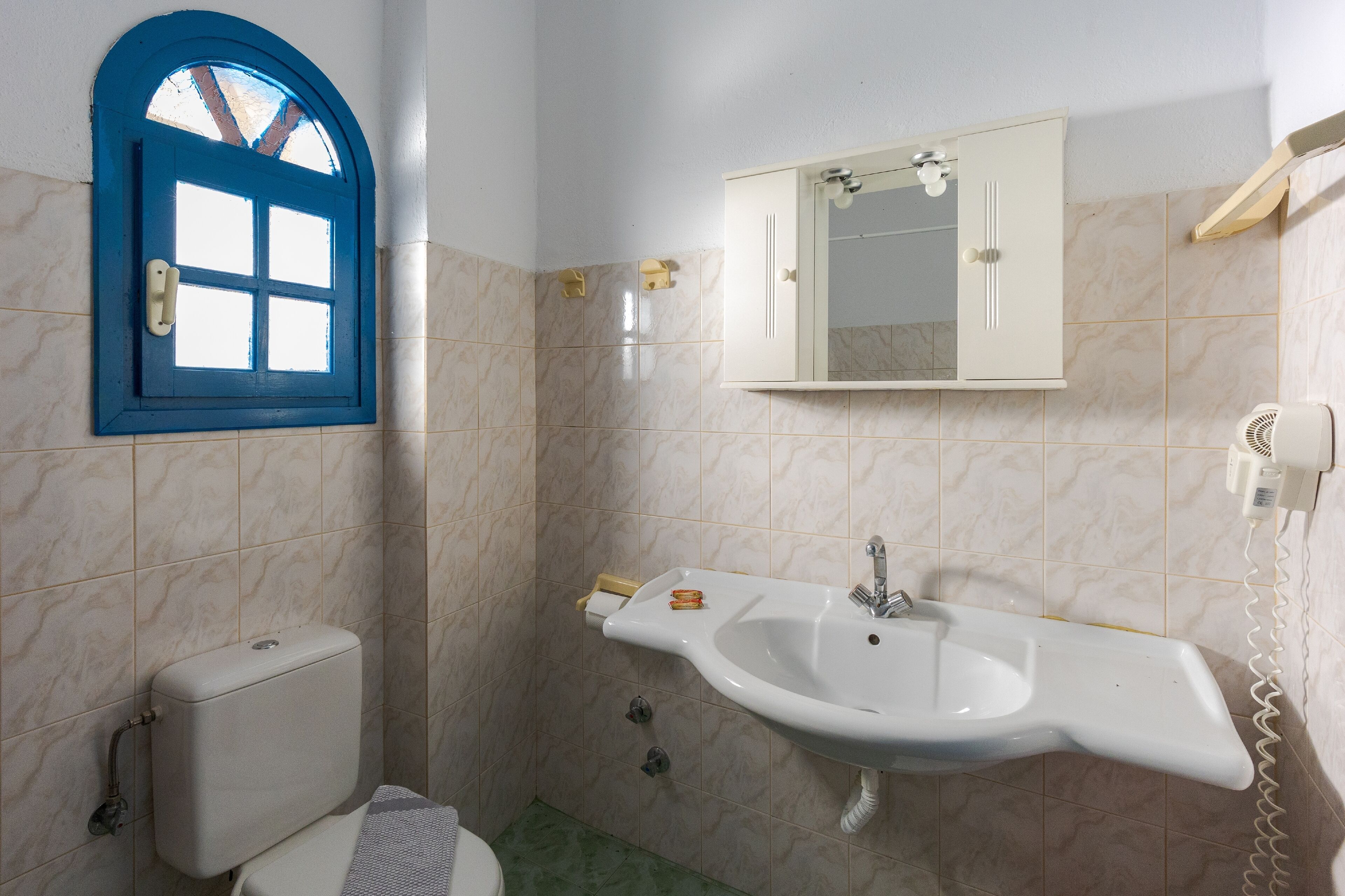 A bathroom with a toilet, a sink, a mirror, and a window with a blue frame.