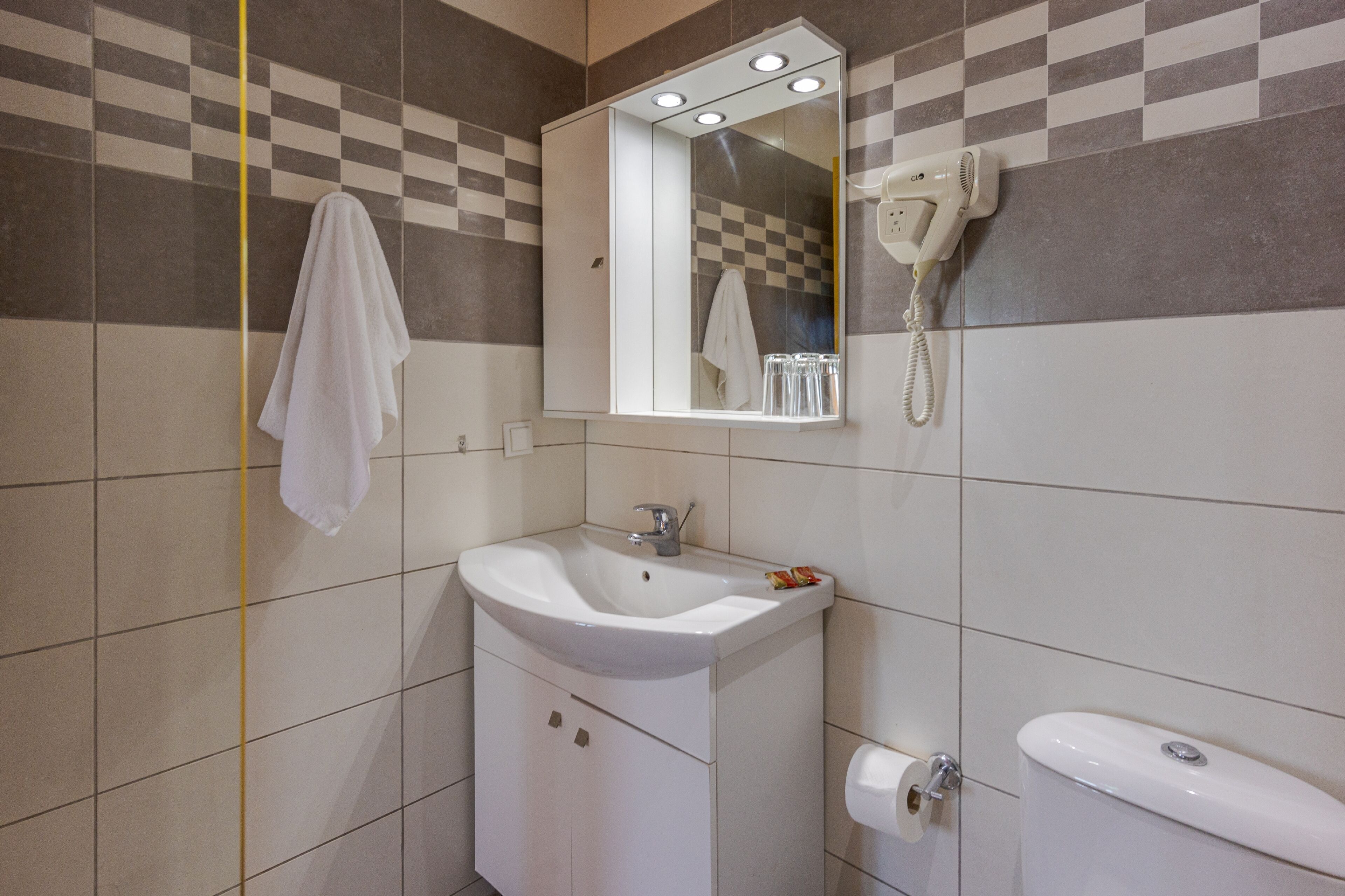 A bathroom with a white sink, mirror, and toilet. There is a towel hanging on the wall and a hairdryer mounted above the mirror.