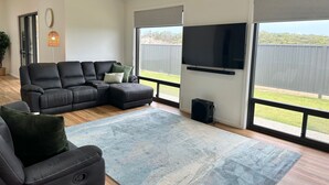 Een moderne woonkamer met een hoekbank, een flatscreen televisie en grote ramen.