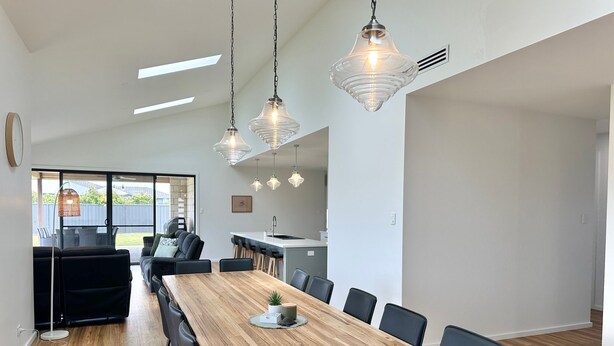 Een moderne keuken met een centraal eiland, een eethoek met een houten tafel en stoelen, en hanglampen.