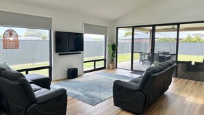 Een moderne woonkamer met een flatscreen televisie, comfortabele zitplaatsen en grote schuifpuien naar een achtertuin.
