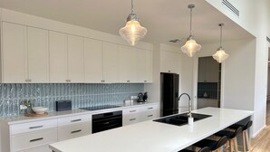 Een moderne keuken met witte kasten, een groot eiland met barkrukken en hangende lampen.