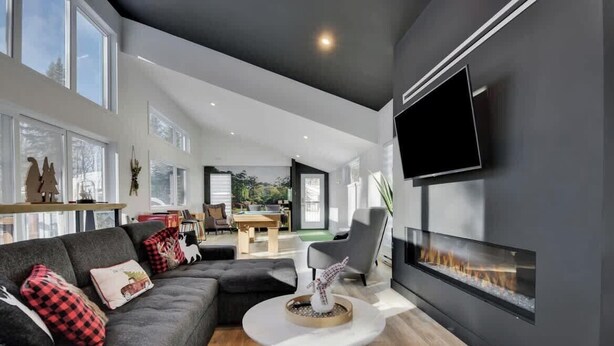 A modern living room with a fireplace, a flat-screen TV, and a dining area visible through an open door.