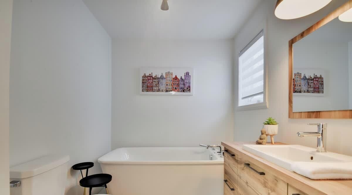 Un baño moderno con bañera, lavamanos, espejo y dos taburetes negros.