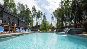 A swimming pool with lounge chairs, a waterfall feature, and a building with a dark facade.