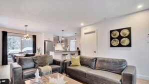 A modern living room with a sofa set, a coffee table, and a dining area in the background.