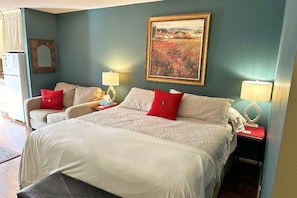 A bedroom with two beds, a sofa, a mirror, and a painting on the wall.