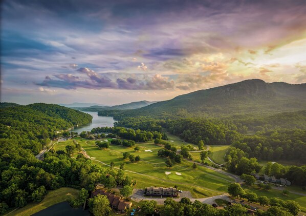 A golf course with a lake, surrounded by forested hills and a mountain in the distance.