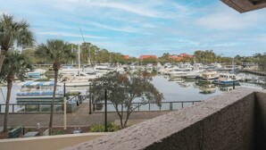 A marina with multiple boats docked, palm trees, and a building with a red roof in the background.