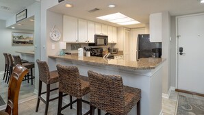 A kitchen with white cabinets, a microwave, a refrigerator, and a bar area with wicker chairs.