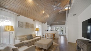 A spacious living area with a wooden ceiling, a sofa, a dining table with chairs, and a television on a wooden cabinet. - Just Six Houses to the Beach in Seaside, FL + 2 Adult Bikes! (Santa Rosa Beach)
