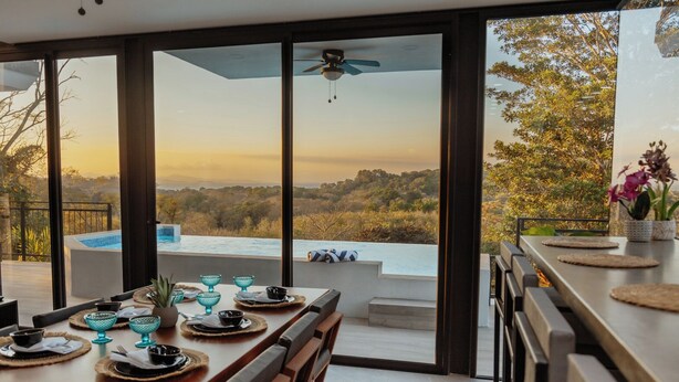 Zona pranzo con tavolo imbandito per quattro, con vista su una piscina e un paesaggio suggestivo.