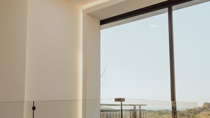 Un interno moderno con un'ampia vetrata, un balcone e vista su un paesaggio naturale.